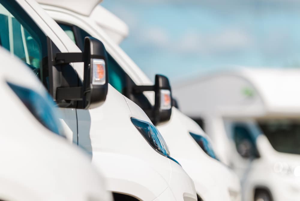 A row of white rvs in a parking lot.