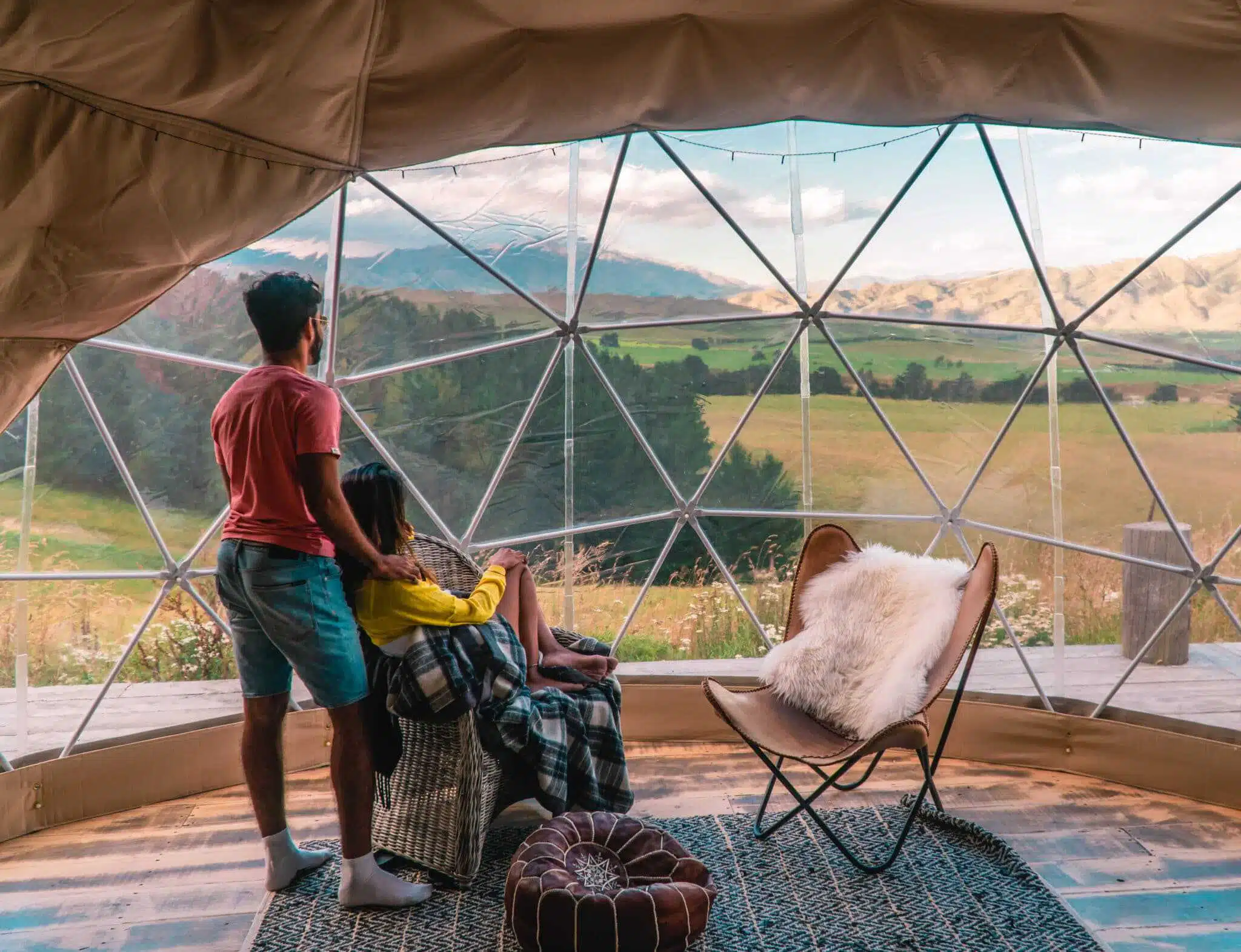 Two people sitting inside a dome tent looking out over a valley.