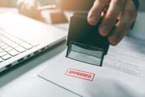 A person is stamping the word approved on a piece of paper.