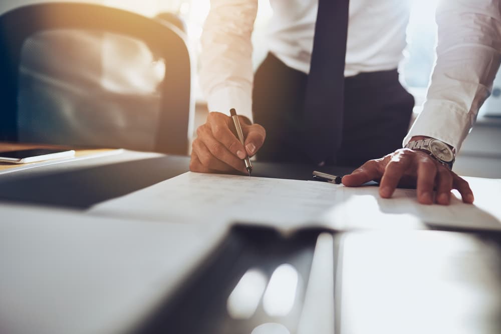 A businessman signing an acquisition agreement document at a desk.