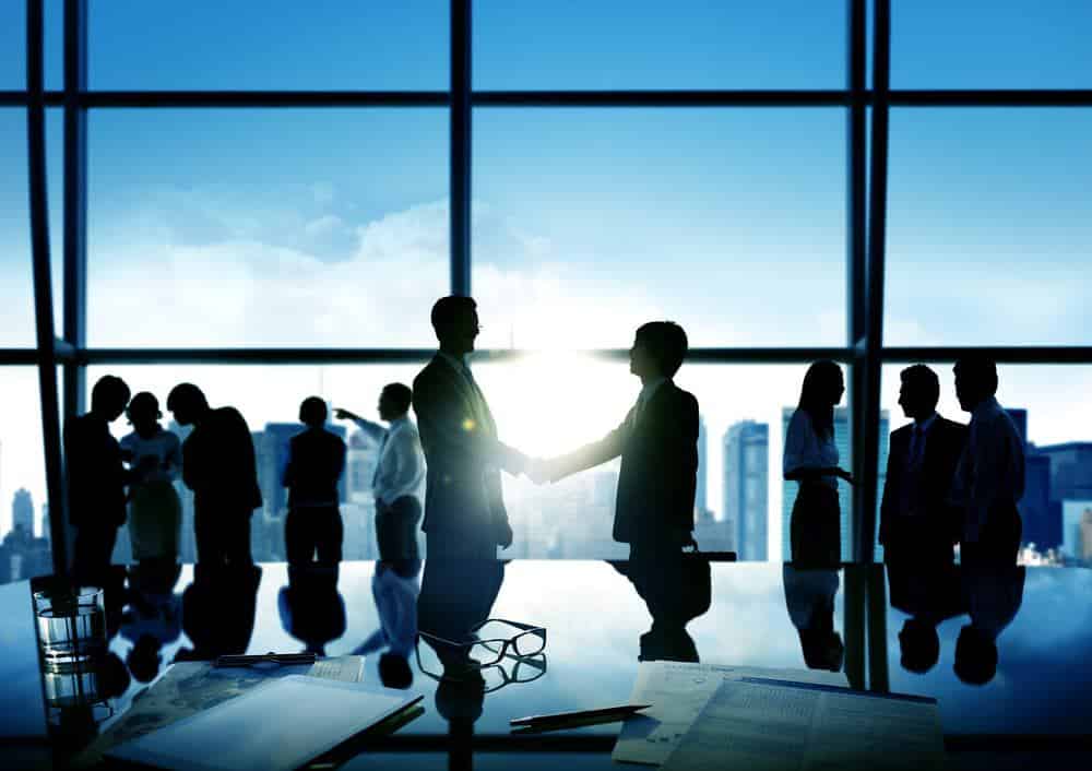 Silhouettes of business people shaking hands in front of a window, representing the partnership between RV Retailer and the GoRollick Dealer Network.