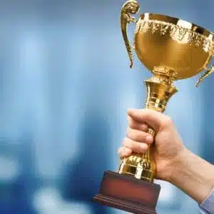 A man holding up a gold trophy in front of a blurry background.