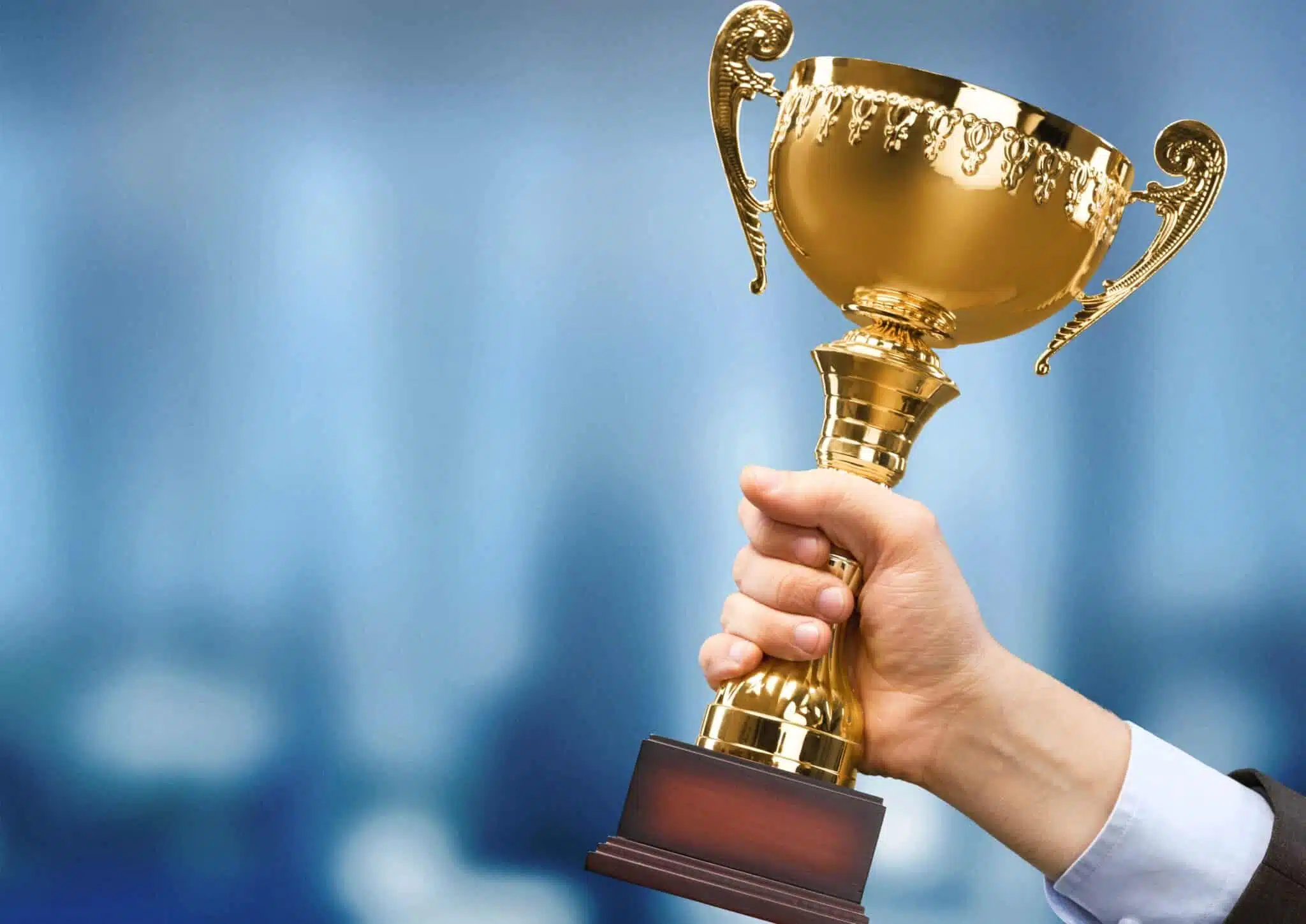 A man holding up a gold trophy in front of a blurry background.