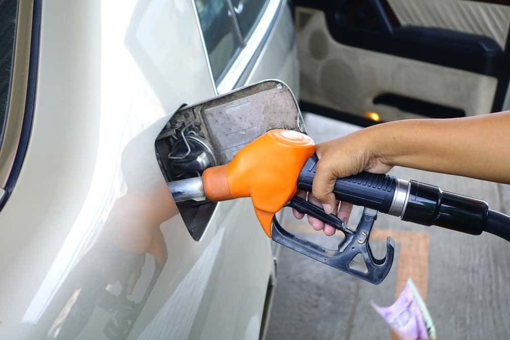 A person is filling up a car at the gas station, concerned with the prices at the pump.