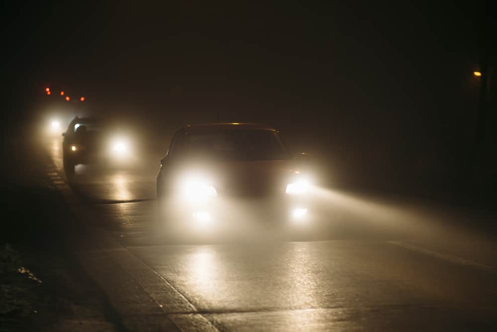 A car with Adaptive Driving Beam Headlights driving on a foggy road at night, showcasing the safety feature recommended by NHTSA for New Vehicles.