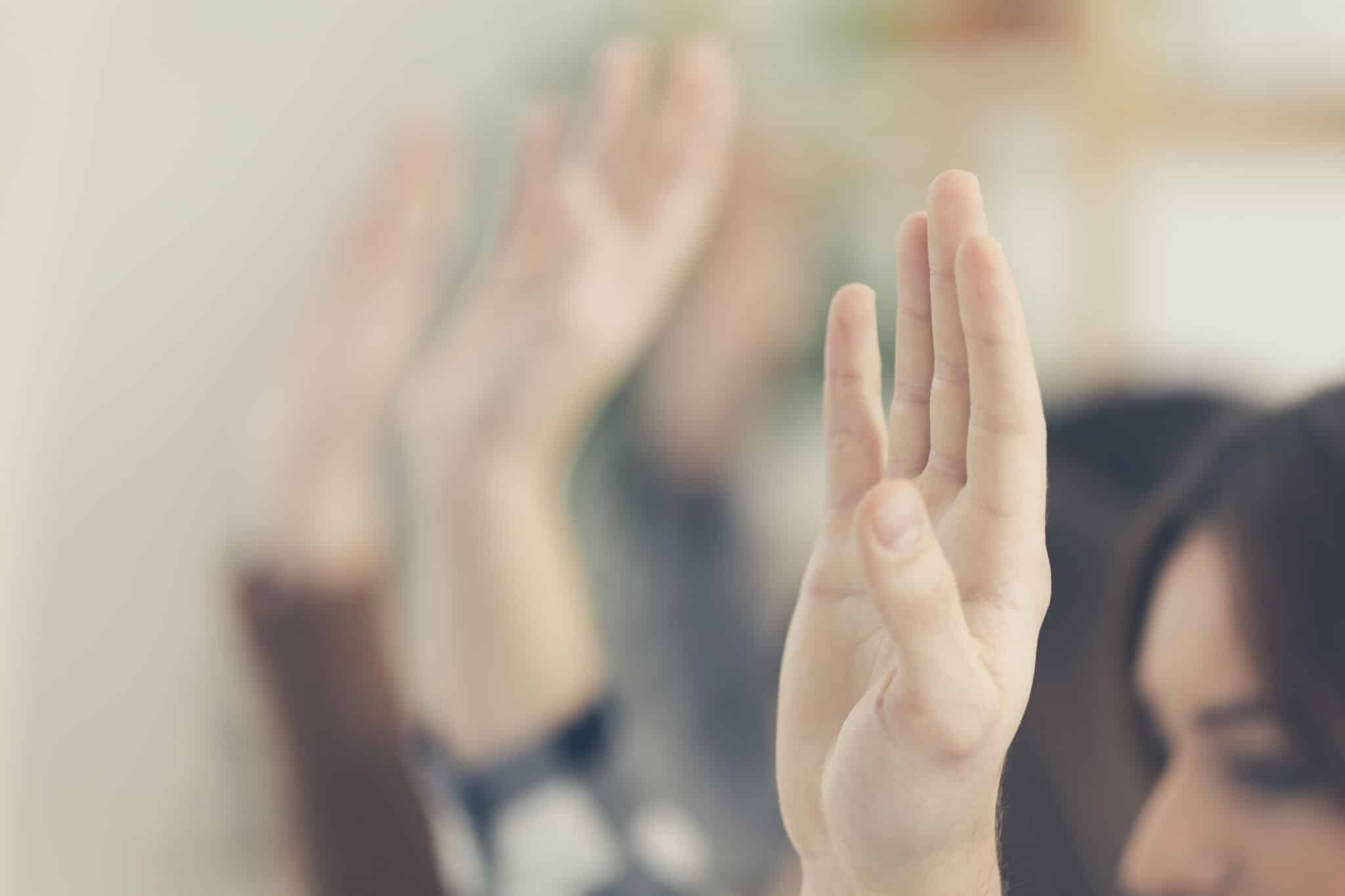 A crowd of people raising their hands in the air during a town hall meeting.