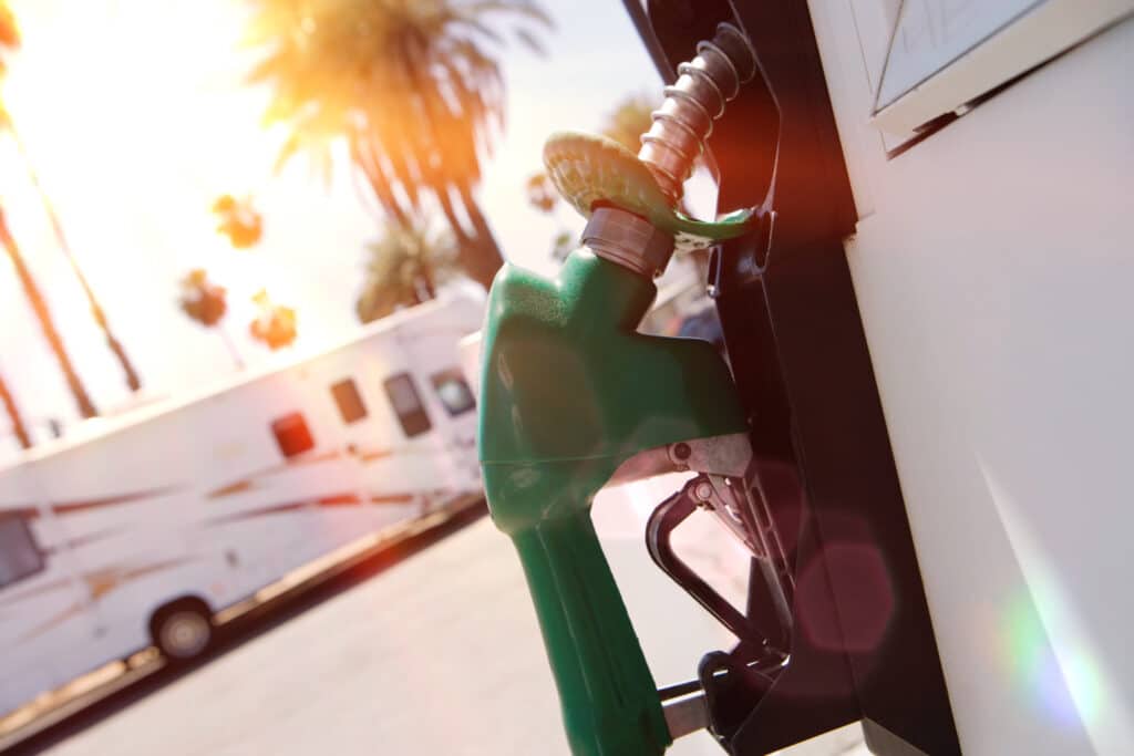 An Australian RV, painted in green, is parked next to a gas pump while considering fuel costs.