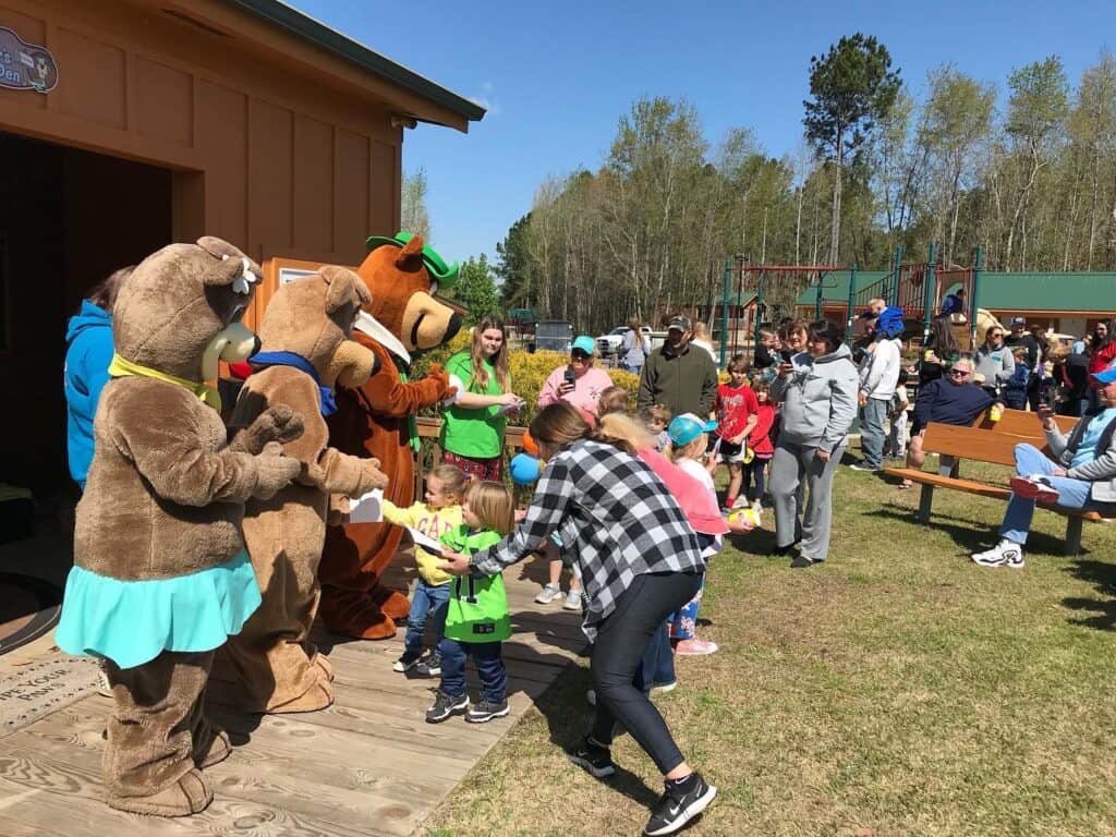 A group of children are standing in front of a building with bear mascots at Jellystone Park.