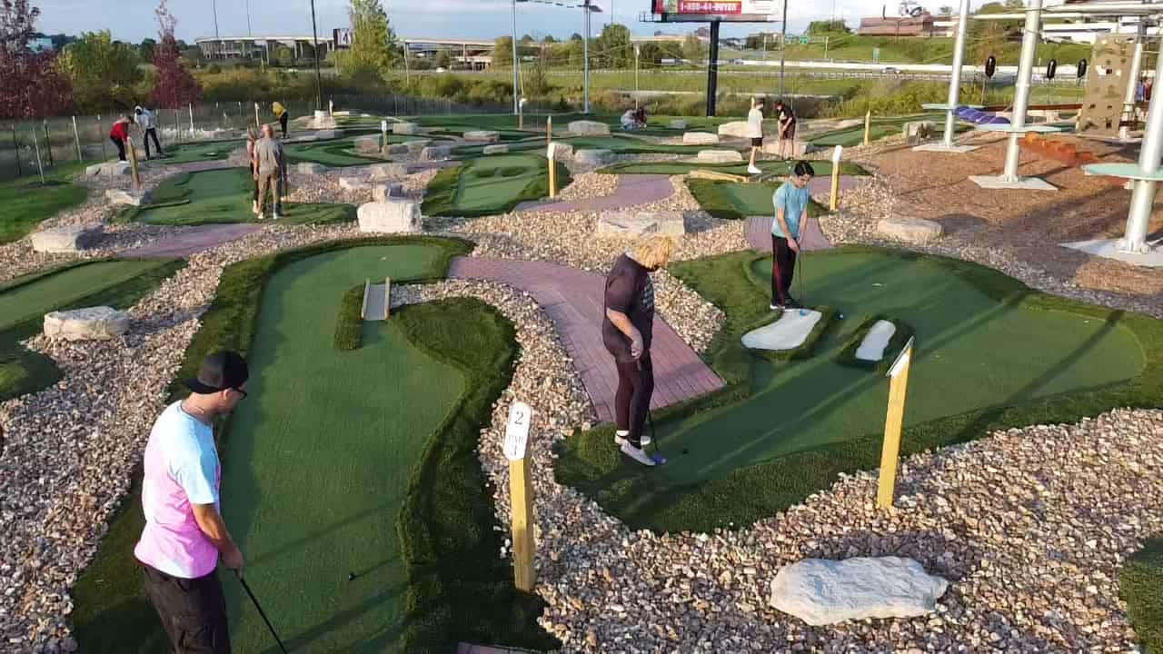 A popular group challenging each other at the AGS Miniature Golf Course in a park.