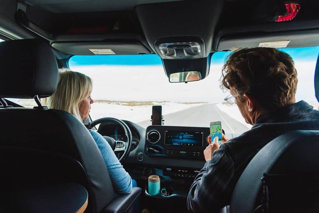 Two diverse people sitting in the back seat of a van looking at their phones.
