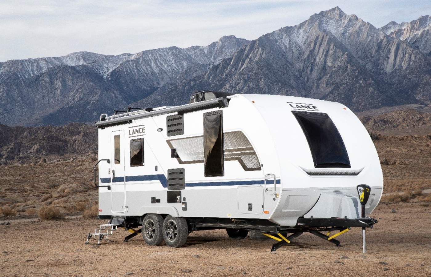 A Lance Camper parked in the desert with mountains in the background.