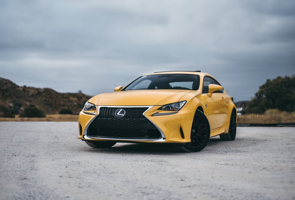 A yellow Lexus RC, awarded with the Best Resale Value Award by Kelley Blue Book for 2022, is parked on a gravel road.