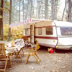 A caravan parked in the woods with a table and chairs, offering a surge of tranquility amidst the serene landscapes of Wales.