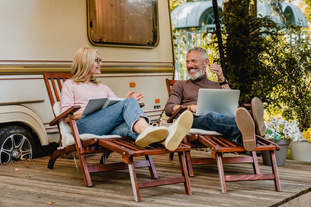 A couple sitting in lawn chairs with laptops in front of an RV making Florida travel reservations.