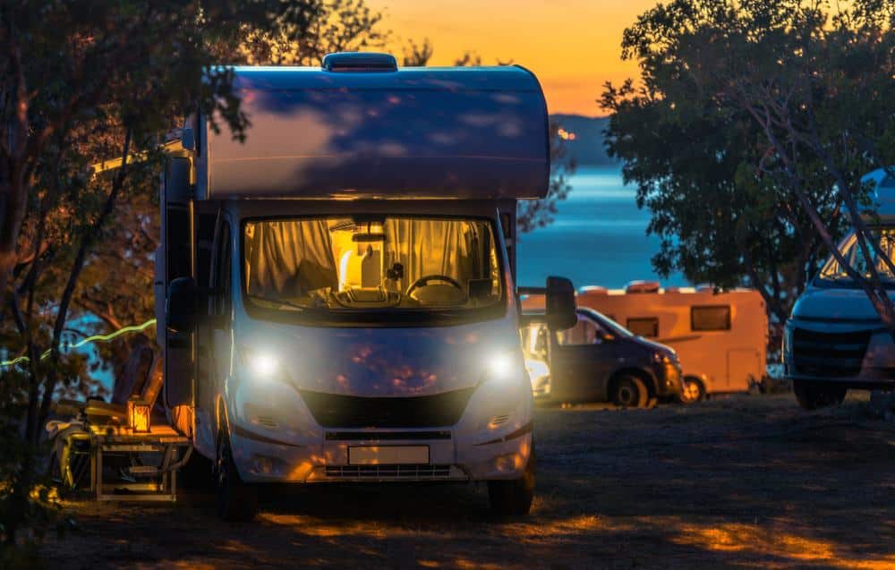 A crowd of RVing enthusiasts enjoy the tranquil setting of a sunset in the woods, while minimizing their travel costs.