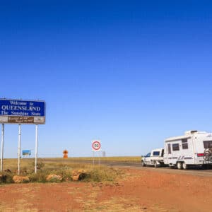 An RV, owned by the Caravan Park owners, is traveling down a desert road with a sign for the CPAQ Conference.