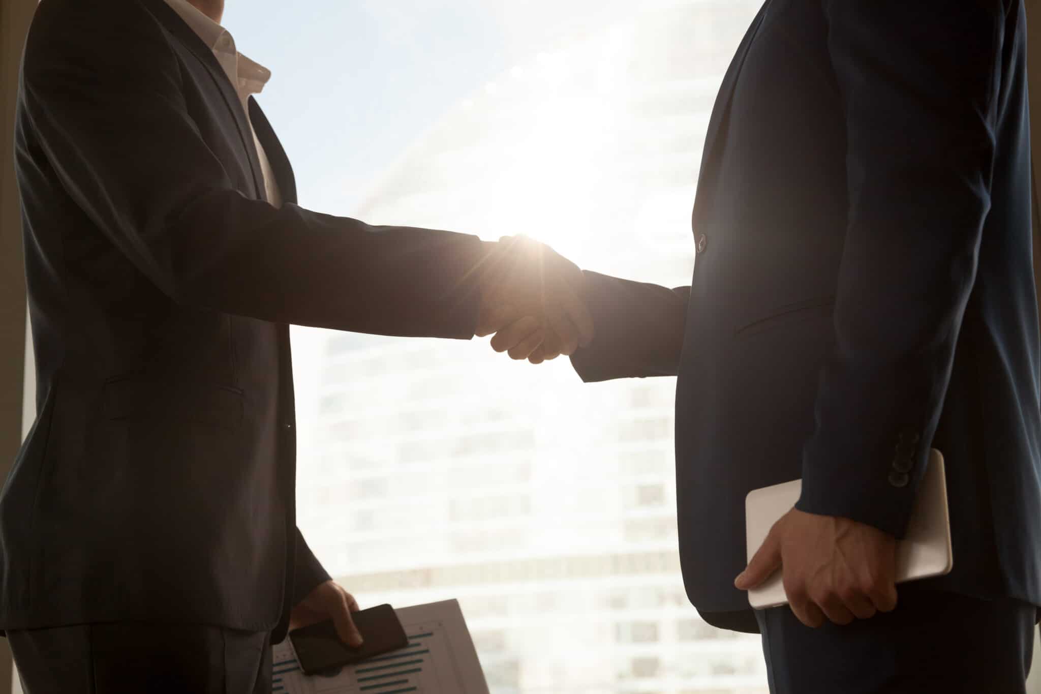 Two businessmen shaking hands in front of a window, representing a successful takeover.