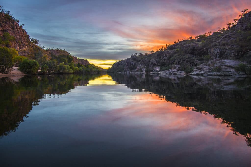 A sunset is reflected in the water of a river at Northern Territory Parks.
