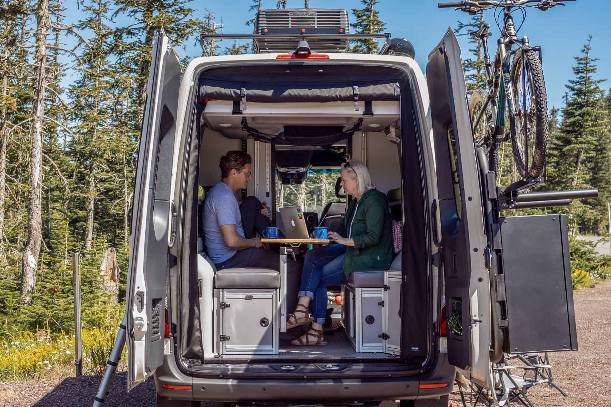 Two people camping in the back of a camper van.