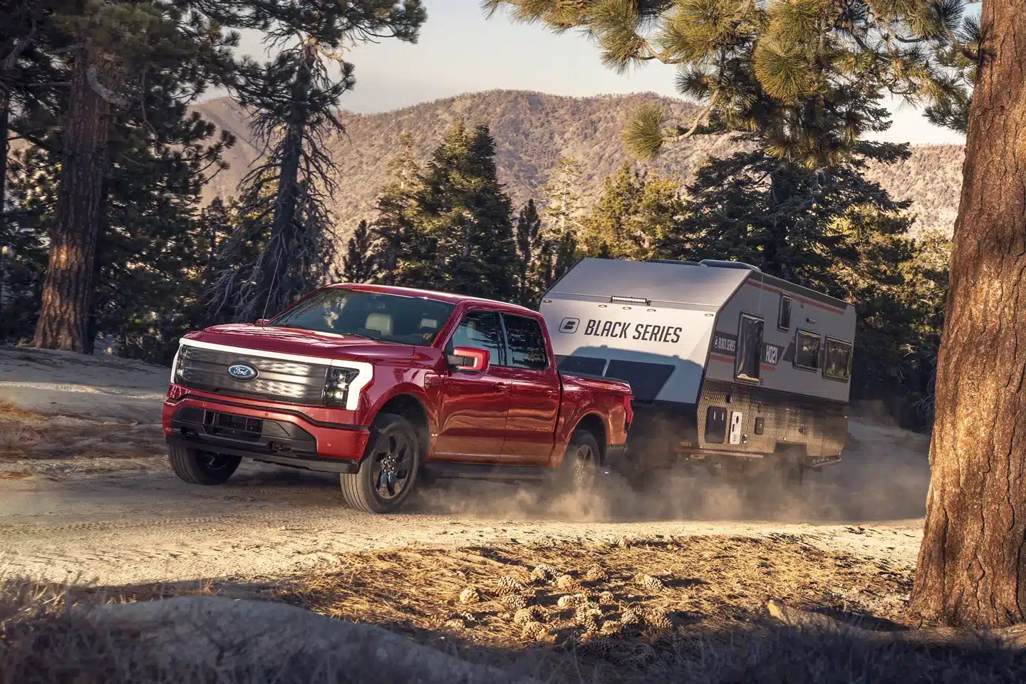 The 2020 Ford F-150 Lightning, an electric vehicle by Ford, is driving down a dirt road with a trailer behind it.