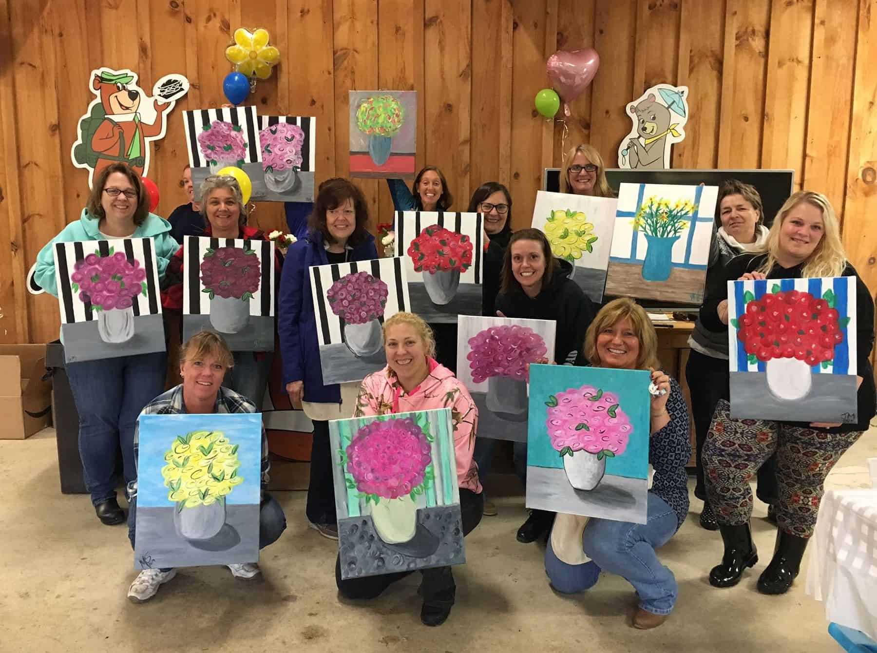 A group of women posing for a picture with flowers at Jellystone Park during Mother's Day Weekend activities.