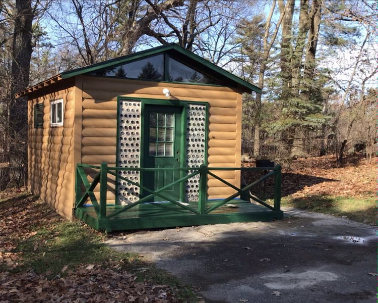 A small cabin in the woods with a green door, nestled within Jellystone Park.