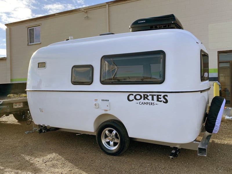 A small white 17-Ft. Cortes Camper parked in a dirt lot.