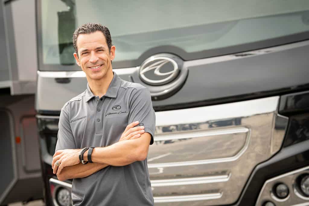 Hélio Castroneves, an Indy 500 Winner, standing in front of a American Coach Luxury Motorhome.