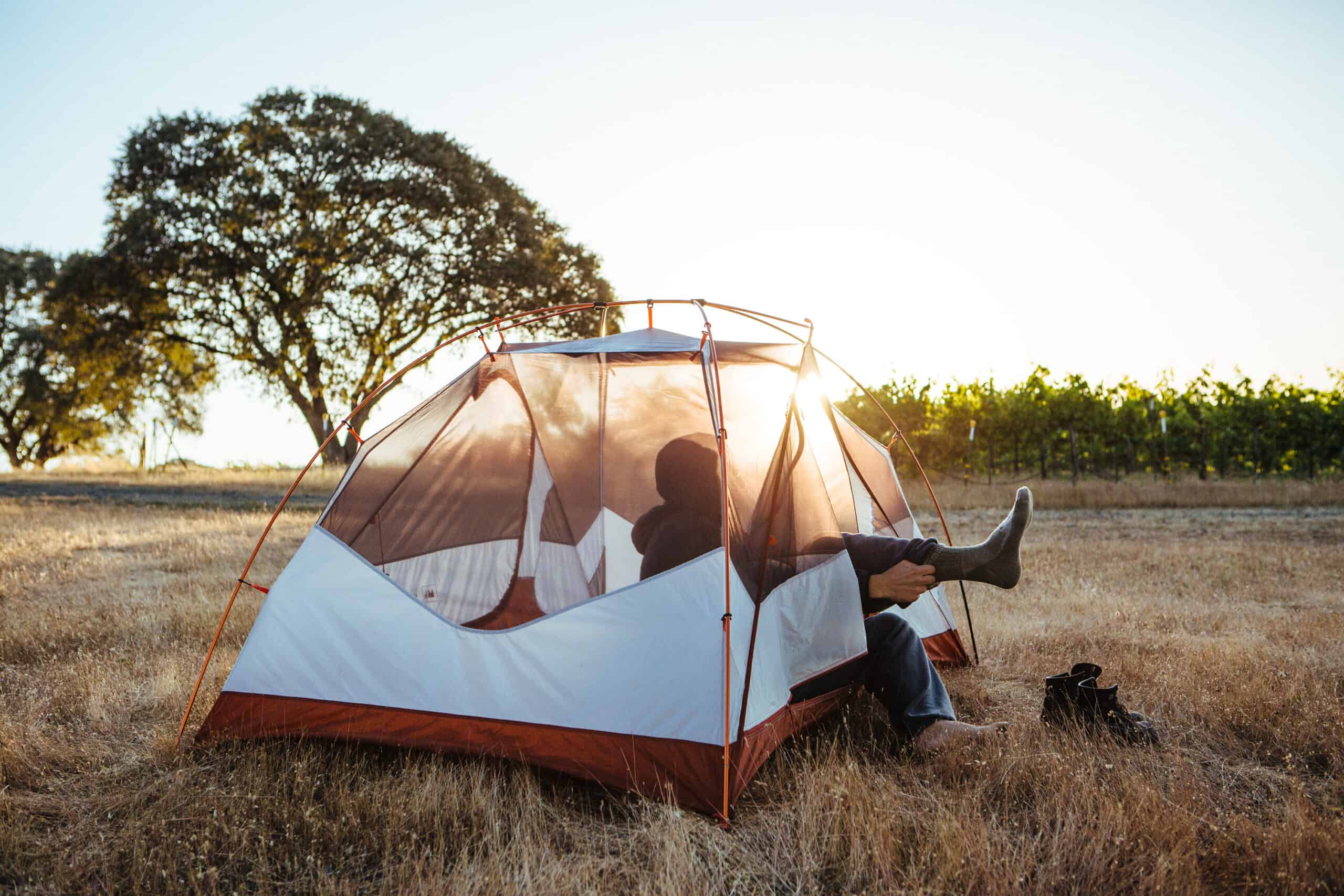 A person enjoying the peace and tranquility of nature while sitting in a tent in a field, embracing the picturesque beauty offered by Hipcamp.