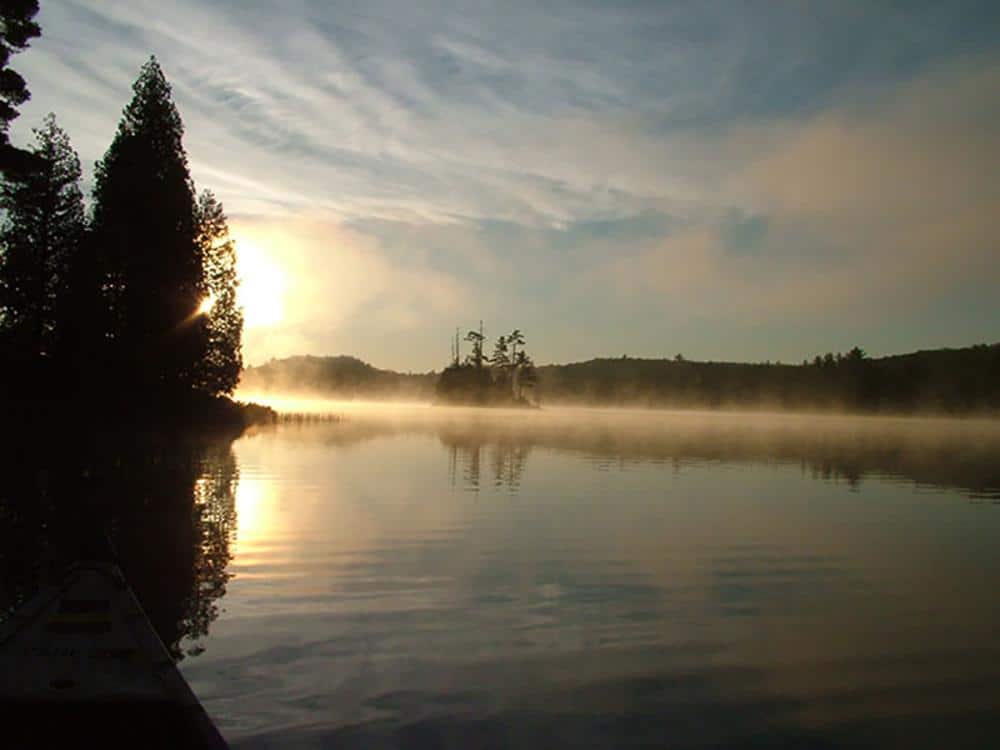 A misty morning scene of a canoe gliding across a serene lake in a picturesque state park in Michigan.