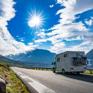 A Roamly-branded rv is driving down a road with mountains in the background.