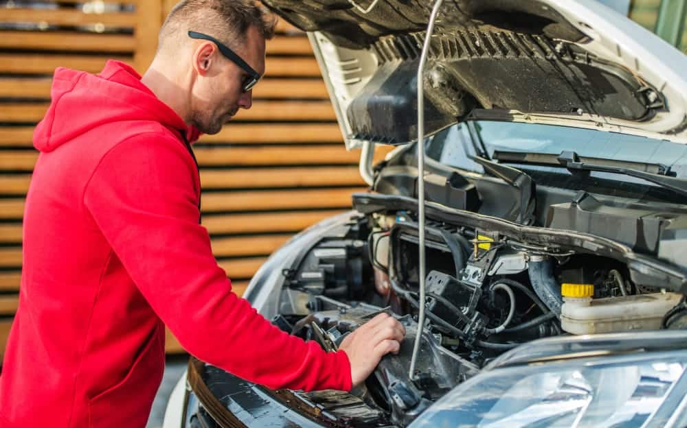 A man performing Battery Maintenance on the engine of a car with the assistance of Pro-Fill and Flow-Rite technologies.