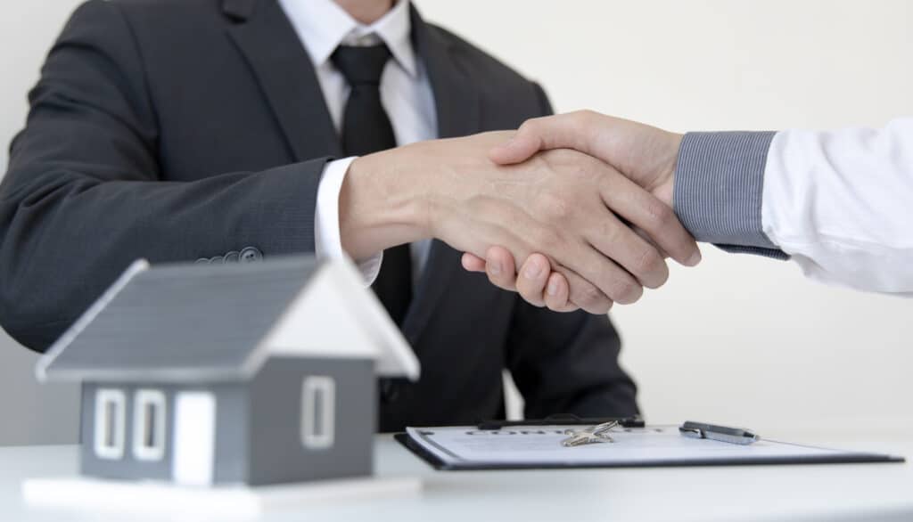 Two businessmen shaking hands in front of a Moray Caravan Parks house model.