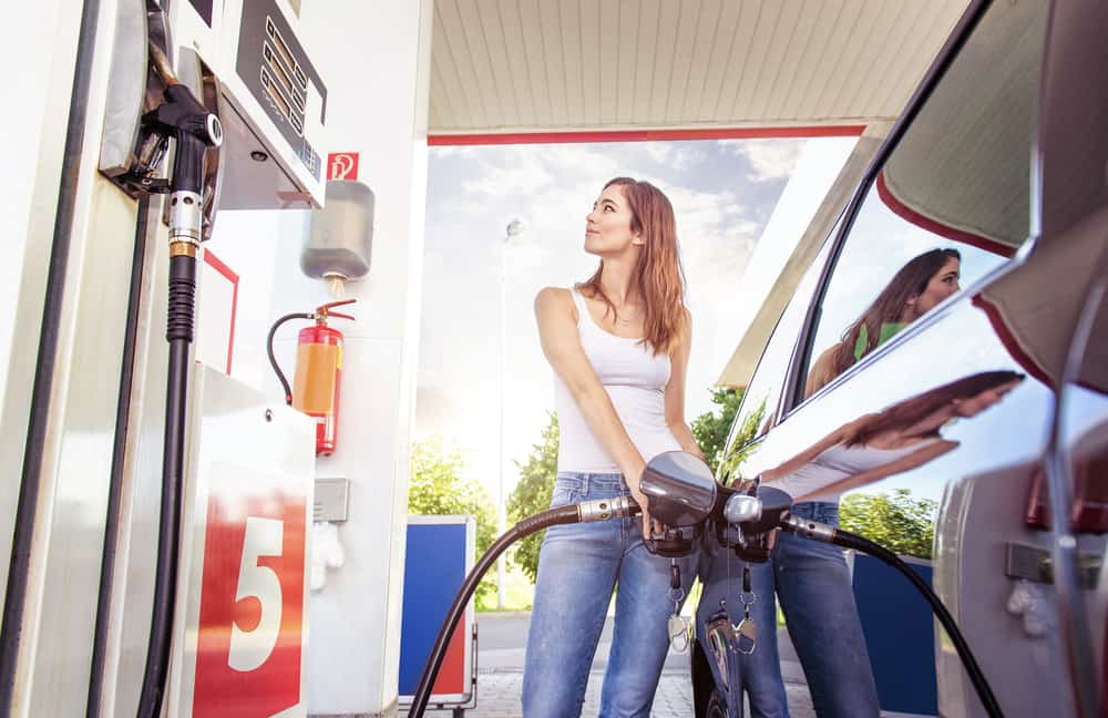 A woman filling up her car at a gas station as she observes the pump prices.