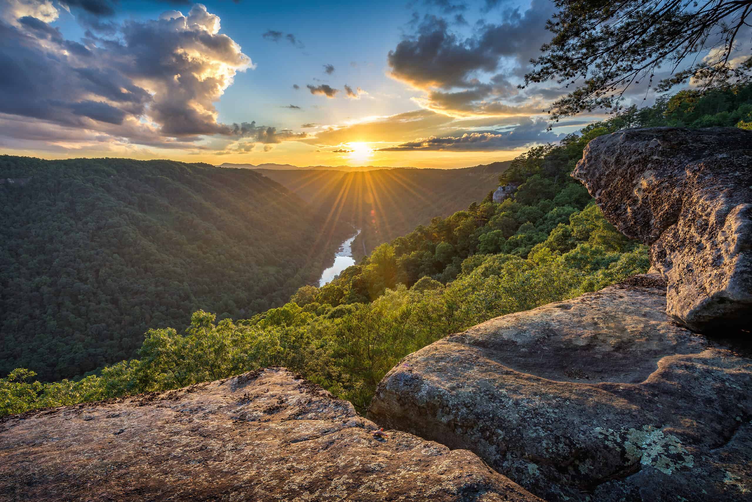 The sun is setting over an Outdoor Heritage Conservation Fund-protected river in West Virginia, surrounded by breathtaking mountains.