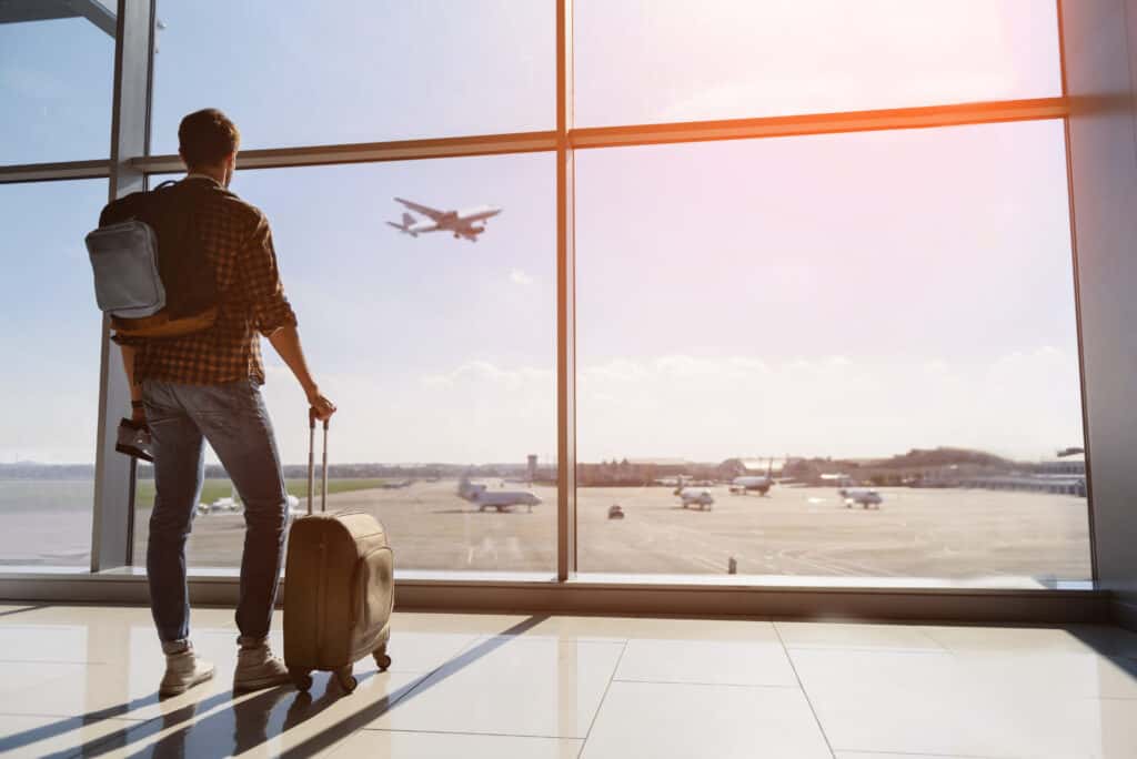 A man with a backpack looking out of an airport window at a US Airlines terminal, as he contemplates a turning point in his life's recovery journey.