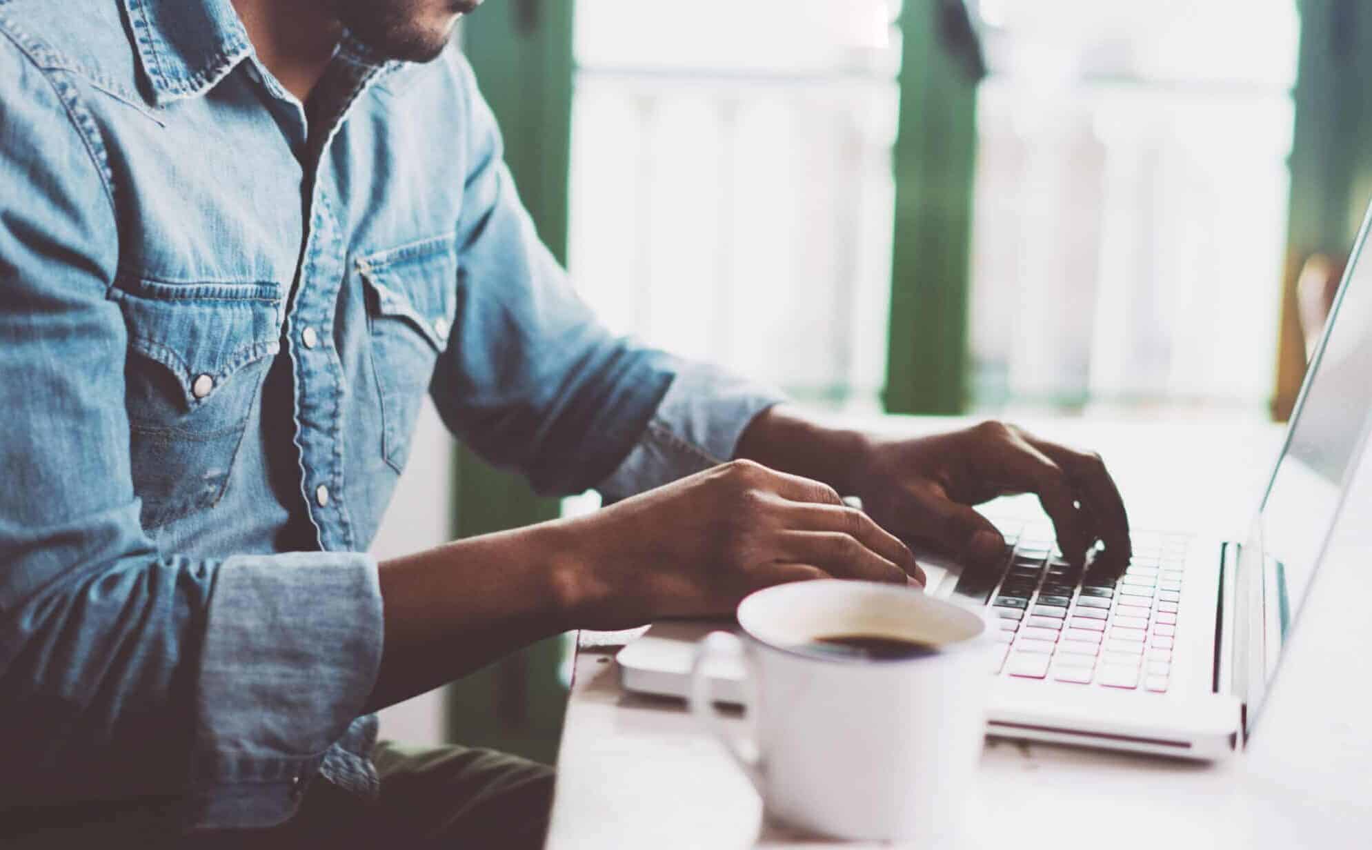 A man typing on a laptop with a cup of coffee while accessing the Forest Service Dashboard.