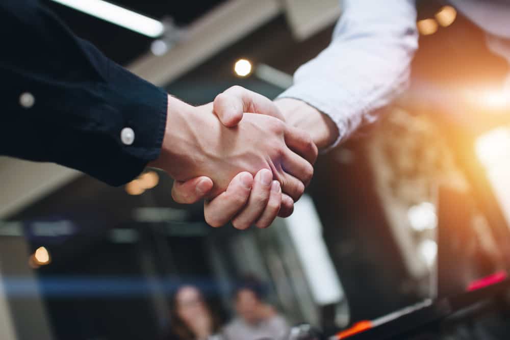 Two business people shaking hands in front of a table, symbolizing the successful business integration of RoverPass and Spot2Nite.