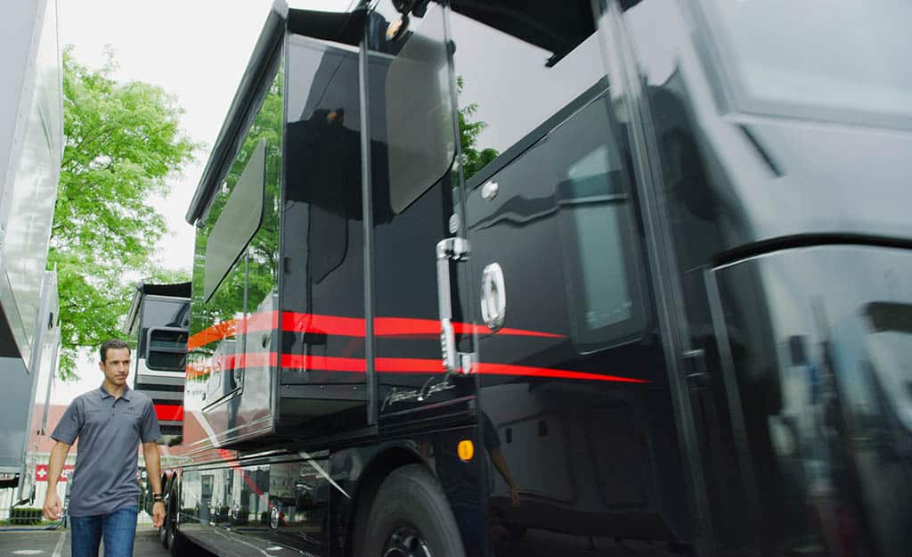 Helio Castroneves, a man standing next to an American Coach RV.