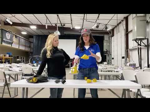 Two women standing at a table in a warehouse, examining electrical adapters and discussing RV basics.