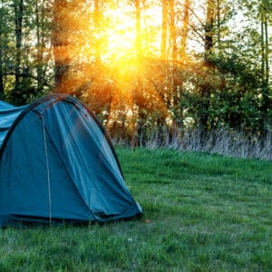 A camping tent set up in a grassy area with trees in the background.