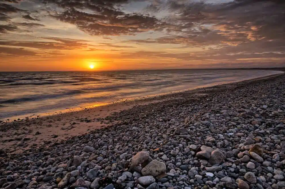 The sun is setting over Horseneck Beach with rocks and pebbles.