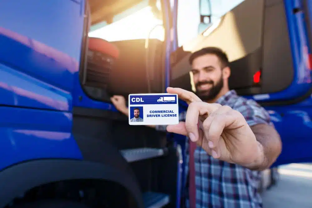 A man holding up a Commercial Driver's License in front of a truck, demonstrating his exemption under FMCSA regulations.