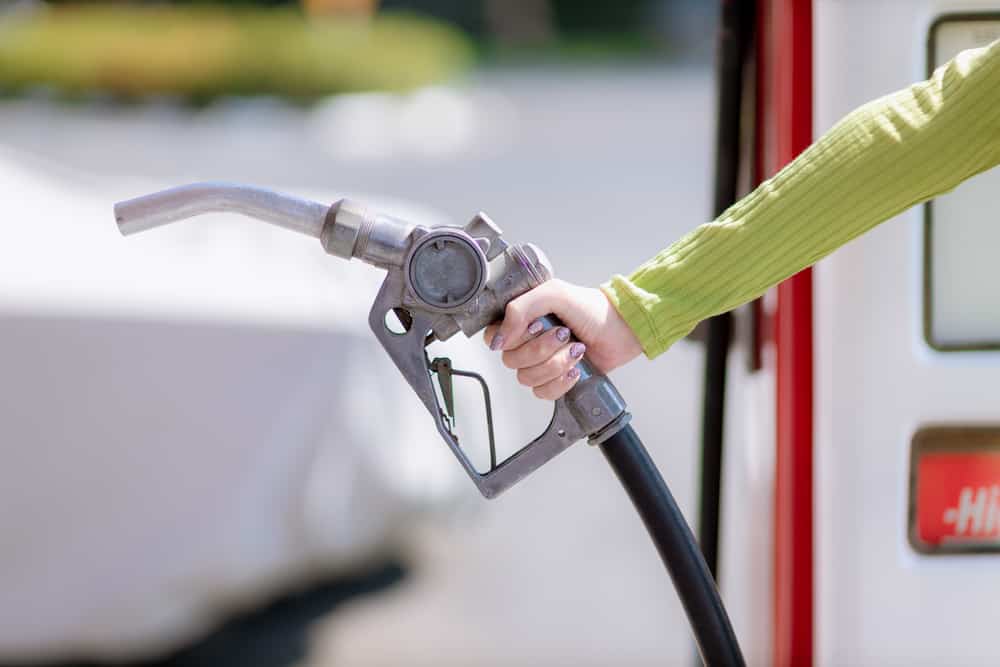 A woman's hand holding a gas nozzle at a gas station, reflecting the rising Gas Prices.