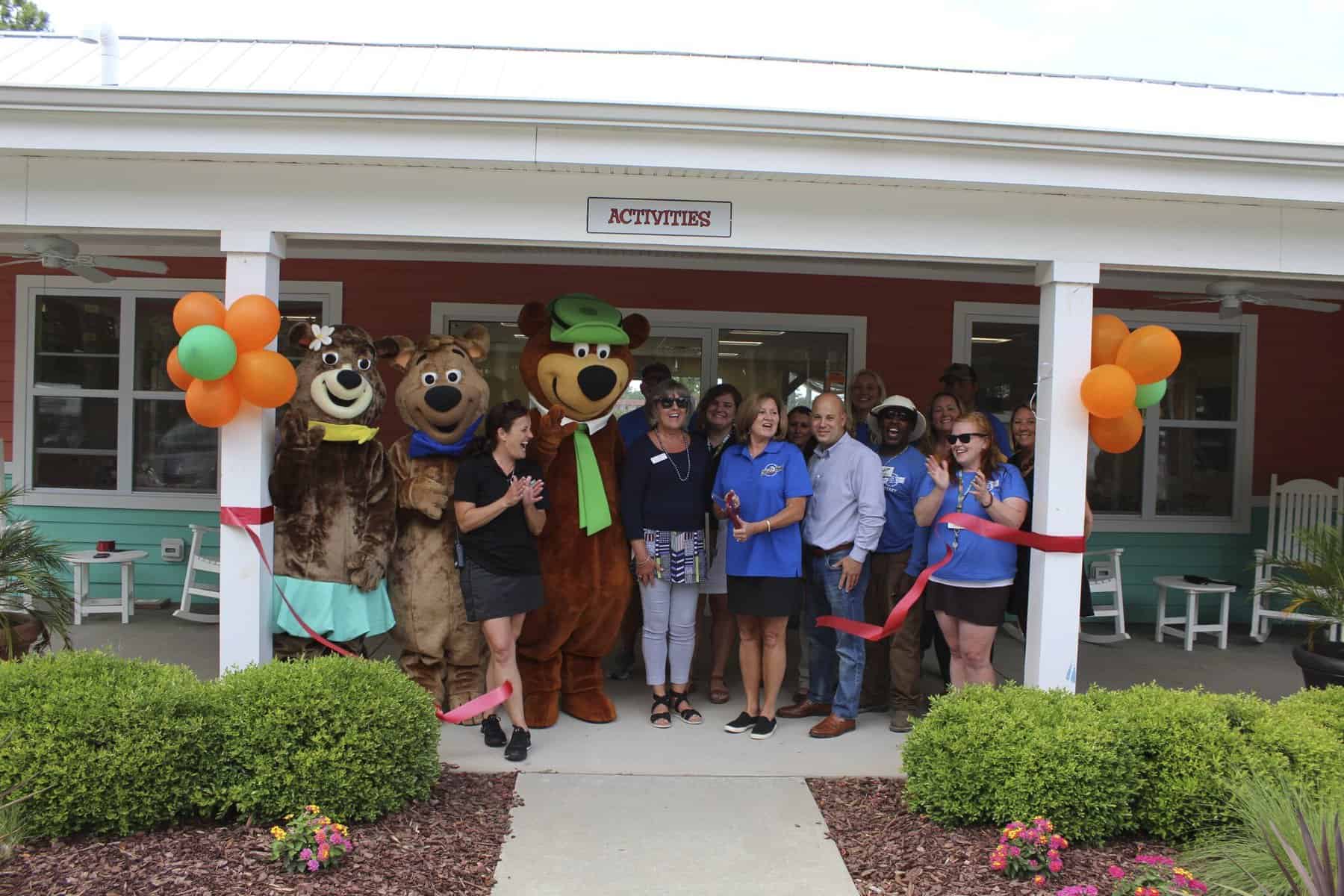 A group of people standing in front of a building at Jellystone Park with bear mascots.