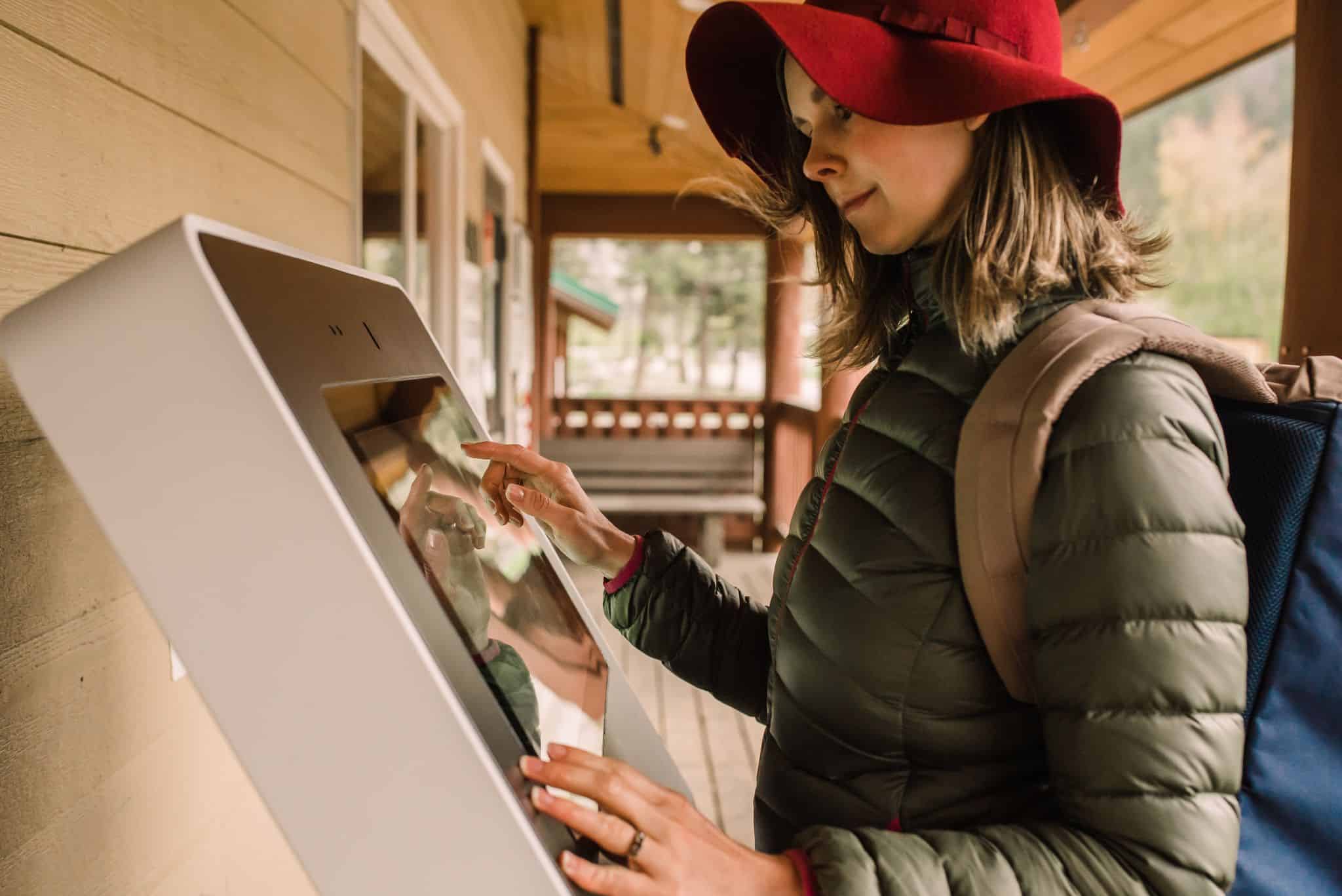 A woman in a red hat is using a Kiosk Concierge to access information at a B.C. Campground.