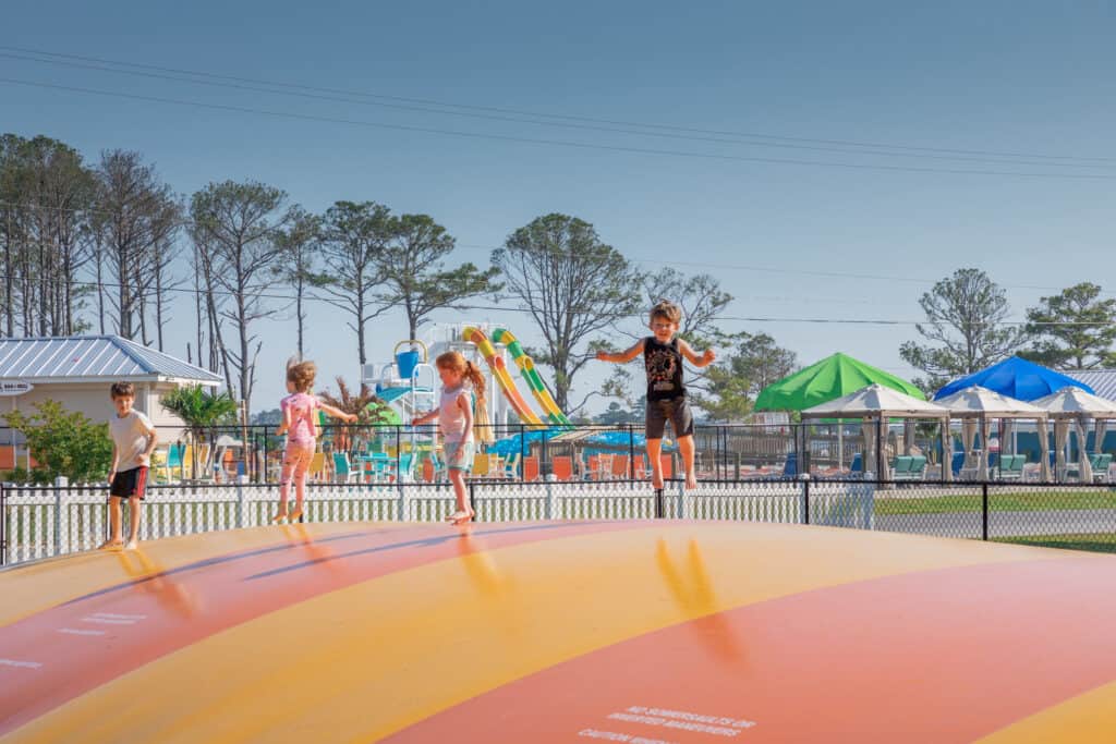 A group of children standing on an inflatable slide at a water park, surrounded by blue water.