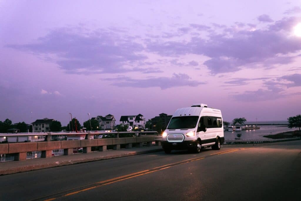 A white van driving on a bridge at dusk.