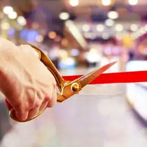 A man performing the grand opening ceremony by cutting a red ribbon in front of a crowd at Carefree Covered RV storage.