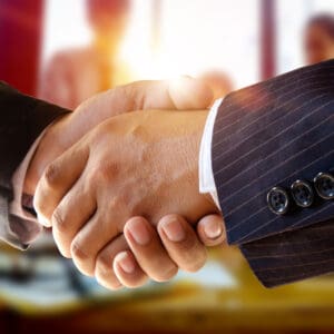 Two business people shaking hands in front of a group of people at Acquires.